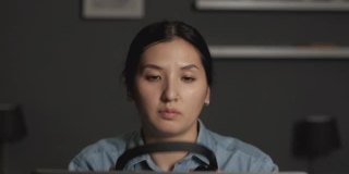 一个年轻的亚洲女人的特写戴着耳机和麦克风的工作，与客户在线视频会议，使用笔记本电脑在一个黑暗的房间在家里