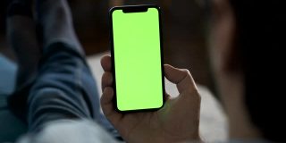 一个男人的手拿着一个绿色屏幕的智能手机看和显示一个新的应用程序，在线工作的特写