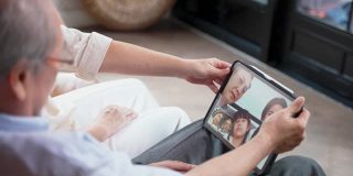 亚洲年迈的祖父母感觉爱和快乐，通过视频电话在家里庆祝虚拟生日，在社交距离，由他们的家人和侄女准备蛋糕。新标准的概念。