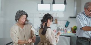亚洲家庭小女孩和祖父母一起在客厅跳舞。儿童和老人和妇女用笑脸感受乐趣。可爱的家庭和活动理念的快乐时刻