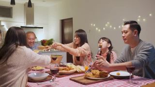 幸福的家庭时间和关系，亚洲大家庭有一个小聚会，一起在家里吃东西。爷爷很高兴看到他的孩子和侄子在家里的餐桌上吃饭，分享食物。视频素材模板下载