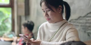 年轻的亚洲美女使用智能手机进行社交媒体，商务，网上购物，转账，金融，网上银行在咖啡厅咖啡厅餐厅在早上的阳光时间。