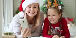 妈妈和女儿用手机和家人朋友一起唱首歌，祝新年快乐。2019冠状病毒感染的肺炎疫情下远程在线圣诞庆祝活动。