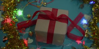 女性双手定型圣诞礼物纸包在桌上。女人正在包装礼物盒，并把红丝带系在蝴蝶结上。
