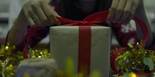 穿红衣服的女孩正在桌子上用红丝带系着蝴蝶结的礼品盒。为新年和圣诞节做准备。