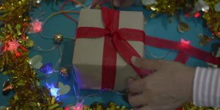 女性双手定型圣诞礼物纸包在桌上。女人正在包装礼物盒，并把红丝带系在蝴蝶结上。