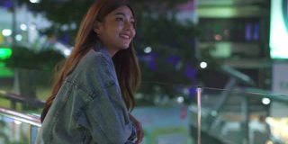 微笑的年轻美丽的亚洲女性游客走在城市的夜晚，看着路灯照明。快乐的漂亮女孩享受和享受城市夜生活的乐趣。
