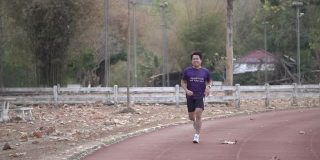 一名亚洲男子在户外运动场上的跑道上跑步。