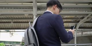 自信的亚洲商人，西装革履的办公室职员在城市中行走，用智能手机在线发短信。办公区内使用手机进行网上办公的商人