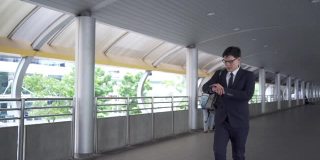 自信的亚洲商人办公室职员，穿着西装，背着双肩包走在高峰时间的火车站上班早上。商务人士急着去城市办公区上班