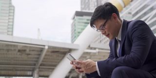 自信的亚洲商人办公人员坐在城市办公区，使用智能手机和互联网进行户外在线工作。无线网络技术与企业经营理念。