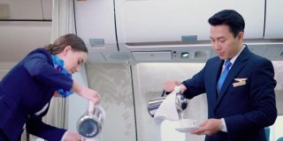 白种人工作人员在飞机上为亚洲年轻夫妇提供饮料。