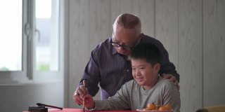 亚洲华人小男孩向他的祖父学习写中国书法