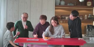 亚洲华人家庭在红纸上书写中国书法，以求繁荣，准备中国新年的家庭装饰