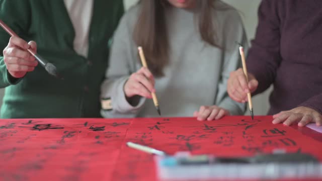亚洲华人家庭在红纸上书写中国书法，以求繁荣，准备中国新年的家庭装饰