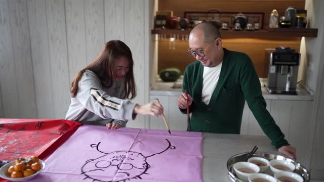 亚洲华人家庭在中国新年庆祝期间练习中国书法，家庭装饰一张红色的纸