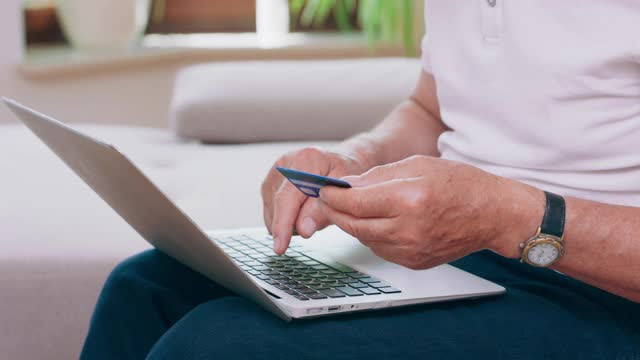 一个在笔记本键盘上打字的手的特写。一位老人用他的借记卡用他的笔记本电脑在网上支付一些东西
