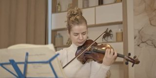 年轻的金发女人拉小提琴与音乐站在豪华的家庭内部