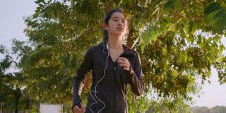 迷人的亚洲少女听音乐，同时在公园里跑步。年轻女子晨跑锻炼。