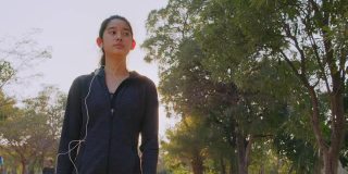 迷人的亚洲少女听音乐，同时在公园里跑步。年轻女子晨跑锻炼。