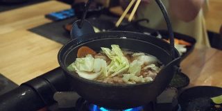 在一家日本餐馆里，一位妇女用筷子把花椰菜放进了涮锅里。