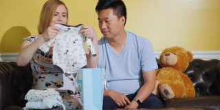 一位怀孕的妇女和她的丈夫看着那些给婴儿买的东西。怀着孩子，给孩子买衣服