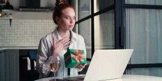 快乐的年轻女子打开礼盒与礼物，同时有视频电话上的笔记本电脑。
