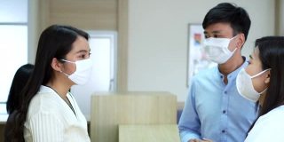 亚洲男性患者戴着医用口罩在现代医院大堂向女医院前台和专业医生询问治疗信息。医院和医疗保健理念。