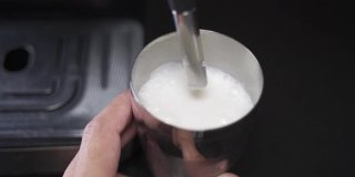 咖啡师用慢动作蒸牛奶。蒸汽棒加热牛奶。错误溅起牛奶。工作失败洒了牛奶。