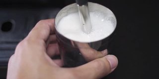 咖啡师用慢动作蒸牛奶。蒸汽棒加热牛奶。