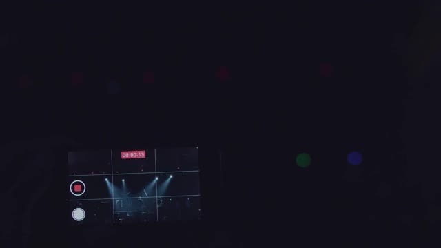 一个男人的手的特写镜头正在为一个乐队在夜店的霓虹灯舞台上表演录像。