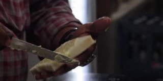 在当地餐馆里，一名印度男子用锋利的刀在白面包片上涂酥油，准备制作素食三明治