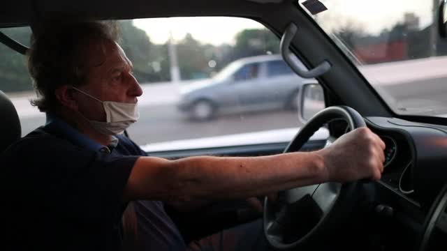 老年人开车时看后视镜，并戴着covid-19口罩