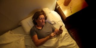 老妇人睡前躺在床上使用智能手机