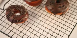 烤架上的甜甜圈涂上巧克力奶油或糖霜。女人手里放了一个甜甜圈
