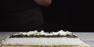 寿司师傅手的特写把螃蟹放在海苔叶和蟹肉上。寿司制作过程。卷寿司卷