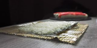 厨师的手把芝麻撒在由内而外的寿司上。戴着黑手套的日本厨师正在准备三文鱼和鳄梨寿司卷