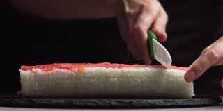 厨师用刀在石板上切寿司卷。-低角度拍摄。美丽的女性手切寿司