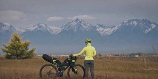 这个女人在混合地形上旅行，骑自行车旅行。旅行者带着自行车包旅行。体育旅游bikepacking。