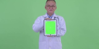 亚洲男子医生的肖像微笑和显示数字平板电脑与复制空间的绿色背景