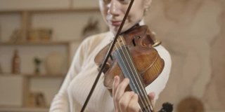 年轻的金发女人拉小提琴的特写，极简主义的家庭内部