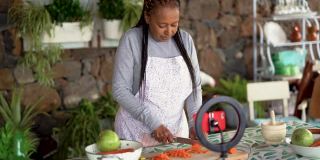 快乐的非洲资深女性用智能手机在网上直播，并引领着户外烹饪