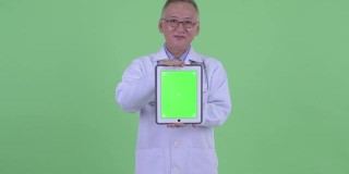 亚洲男子医生的肖像微笑和显示数字平板电脑与复制空间的绿色背景