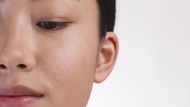年轻的亚洲女子卷她的睫毛，使用特殊的卷发器，近半脸肖像，白色的工作室背景