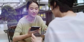 两个亚洲女人在咖啡店聊天。带着微笑和幸福。在你的智能手机网上购物放松你的假期。人们的社会关系