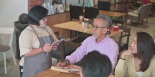 患有唐氏综合症的亚洲女性服务员在咖啡馆用平板电脑为顾客点餐时竖起大拇指