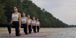 沙滩瑜伽组，女子在沙滩上排队练习瑜伽，女子团队健康生活方式