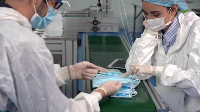 口罩工厂的员工正在使用平板电脑输入来操作机器。口罩工厂的员工在现代工业机器上检查产品质量。