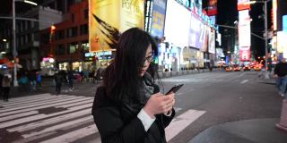 亚洲女性晚上在时代广场使用智能手机