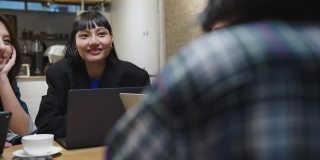 一群快乐的年轻亚洲商务同事使用笔记本电脑在咖啡馆餐厅的团队非正式会议启动项目讨论。
